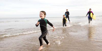 Family fun on the beach Parents and two children wearing wetsuits and running on the beach
