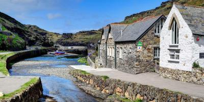 YHA Boscastle exterior and estuary Stone hostel building by a river estuary with a blue sky in the background