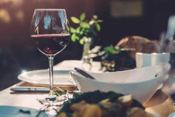 Bowls of food sitting on a table with glasses of red wine