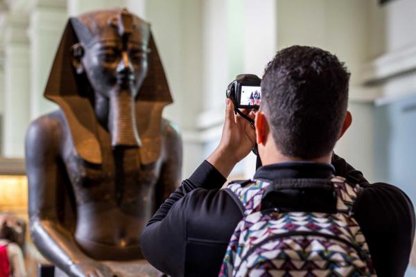 A male tourist taking photo of an Egyptian status brought from Egypt and kept in British Museum of London