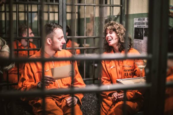 Two people wearing orange jumpsuits behind bars