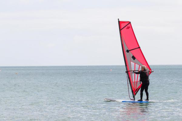 An elderly man keeping active and learning how to windsurf on a calm ocean in Coverack, Cornwall