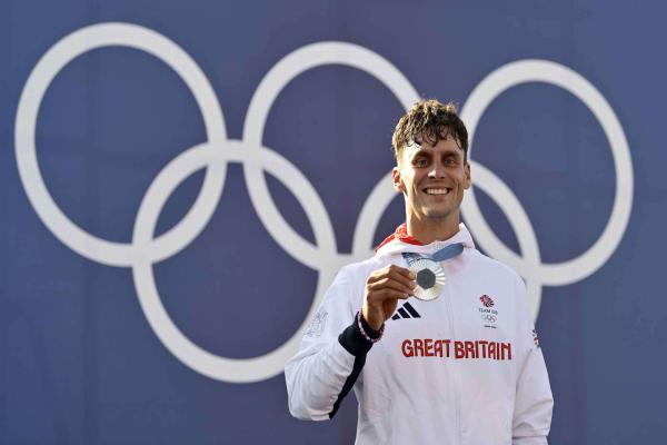 Male athlete holding a medal standing in front of the Olympics logo