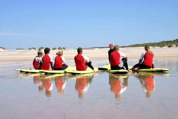 Surfing school, sitting on sand being instructed