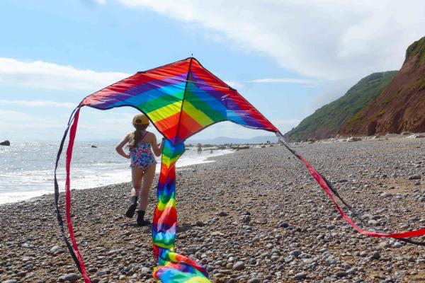 Young girl running on a beach with a rainbow kite