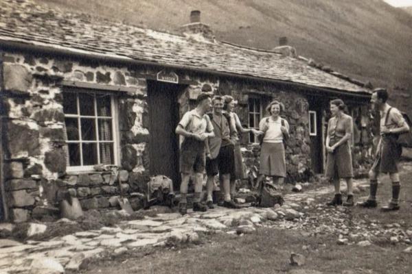 Black and white archive photo of a group of travellers outside a stone hostel building