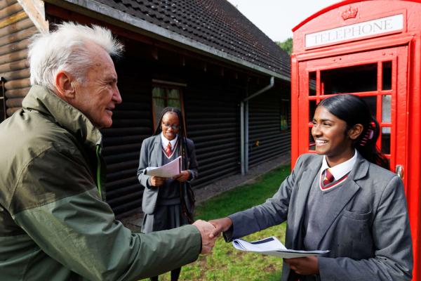 Actor Larry Lamb shaking hands with a school pupil in front of a hostel building