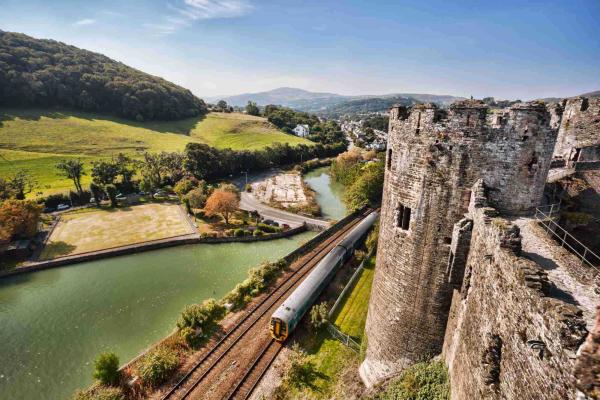 Train travelling past a castle with countryside on the other side of the track