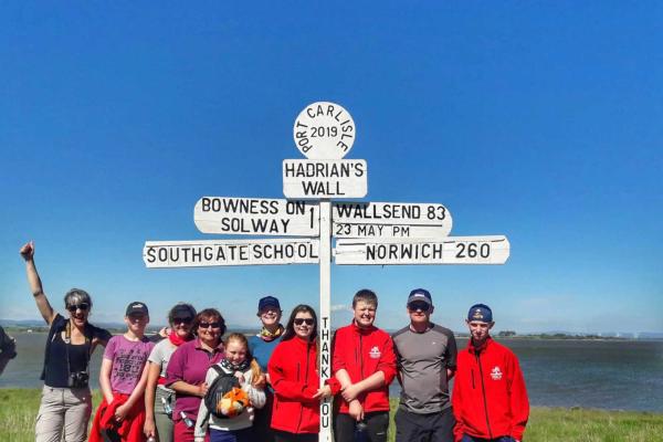 Group of adults and children posting next to a sign for Hadrian's Wall