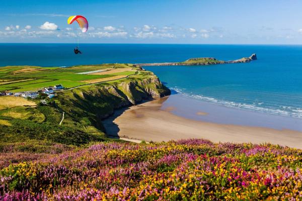 Glider sailing over a beach with blue sea and green cliffs