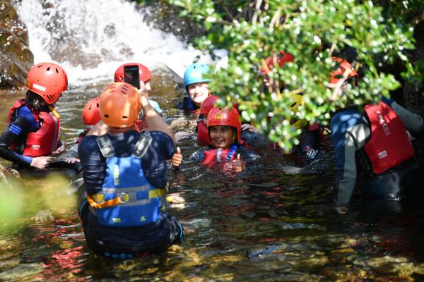 Group of school children in water by a waterfall