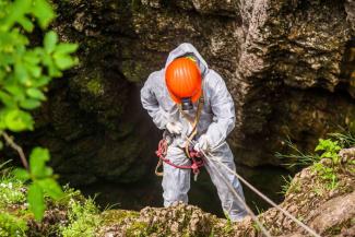 Person wearing an orange hardhat abseiling in a cave