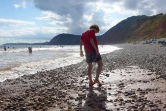 Boy walking in the waves on a pebbled beach