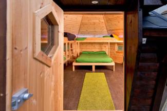 Door open into a wooden cabin with a double bed and bunks