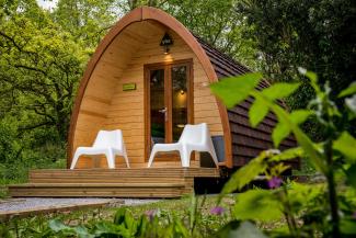 Wooden camping pod with two white plastic chairs on the veranda