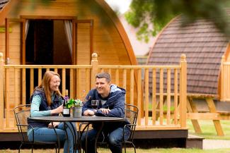 Couple sitting at a table outside a wooden camping pod