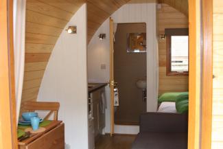 Inside a wooden camping pod with a bed, sofa, kitchenette ane en-suite bathroom