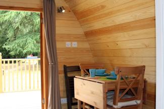 Inside a wooden camping pod with a dining table and a door open onto grass and trees