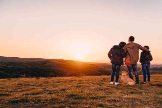 Family with dog embracing at hill and looking at sunset