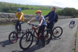 Adult and two children cycling over a bridge