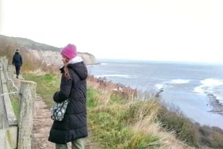 Girl wearing a black coat and a pink hat while walking by the sea