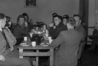 Black and white archive photo of a group of people sitting round a large dining table