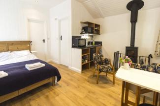 Large, open room with a double bed, kitchenette, table and woodburning stove