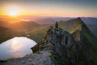 Hiker stood on top of a rocky mountain summit overlooking a lake