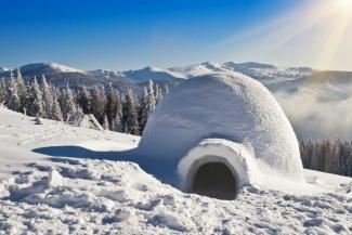 Igloo in the snow with snow-capped mountains in the background