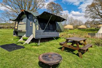 Glamping Landpod on a grass field alongside a wooden picnic bench and a metal firepit