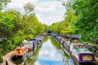 Canal with rows of canal boats surrounded by green trees