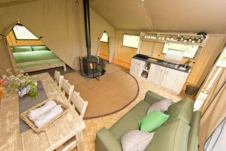 Inside a canvas tent with a two-seater sofa, dining table and woodburning stove