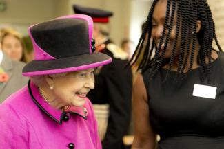 The Queen wearing a pink suit and hat while talking to a member of staff