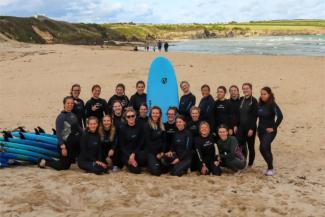 Group of women posing with a surfboard on a beach