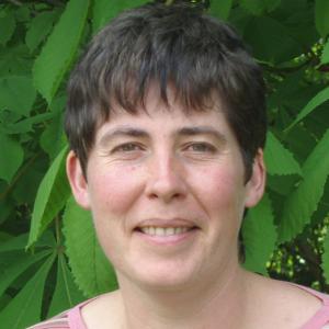 Woman with short hair standing in front of a tree