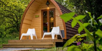 Wooden camping pod with two white plastic chairs on decking