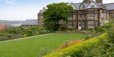 Large mansion building and grounds with stone walls and white wooden window frames