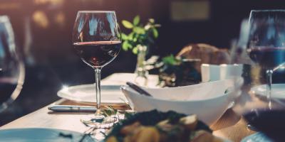 Bowls of food sitting on a table with glasses of red wine