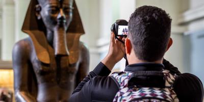 A male tourist taking photo of an Egyptian status brought from Egypt and kept in British Museum of London