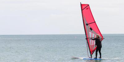 An elderly man keeping active and learning how to windsurf on a calm ocean in Coverack, Cornwall