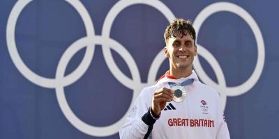 Male athlete holding a medal standing in front of the Olympics logo