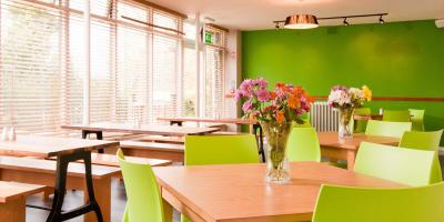 Dining room with green walls, large windows and wooden tables with bench seating and chairs