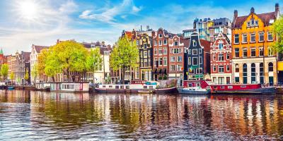 Tall colourful houses along a river with boats and trees