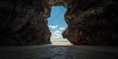 View from inside a large cavern showing a beach and blue skies outside