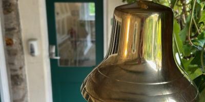 Brass bell hanging in front of a green painted door