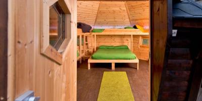 Door open into a wooden cabin with a double bed and bunks