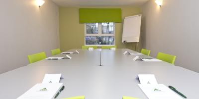 Room with green and white painted walls containing a table and green plastic chairs