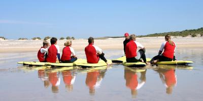 Surfing school, sitting on sand being instructed