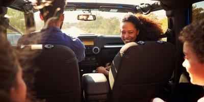 Two adults sat in the front of a car with one looking back at children in the back seats