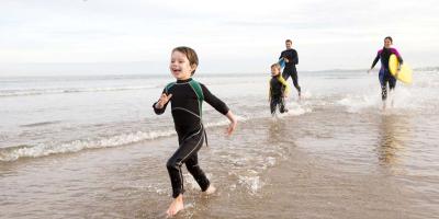 Parents and two children wearing wetsuits and running on the beach